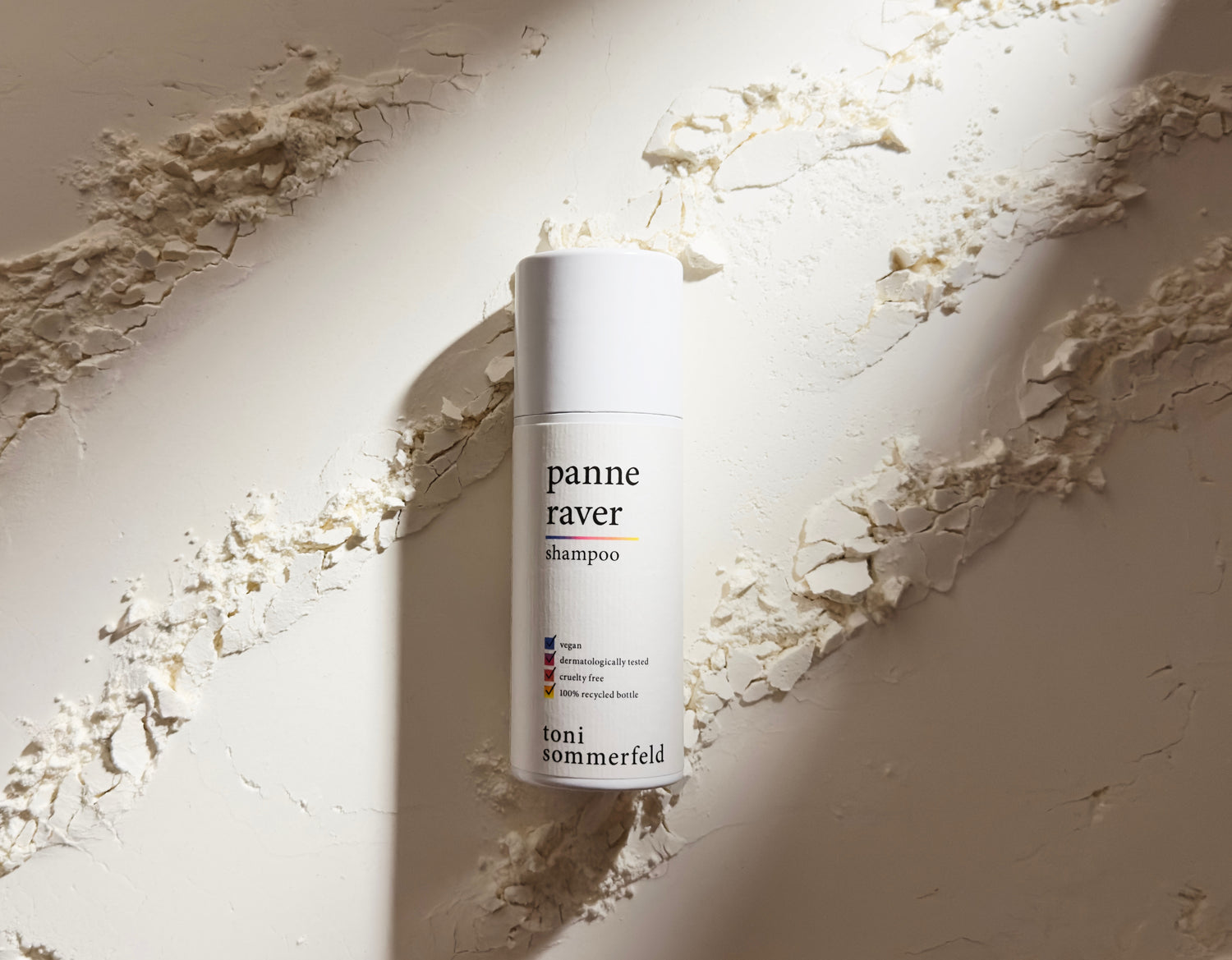 Eine Shampoo-Flasche steht vor einer strukturierten, weißen Wand im Licht.
